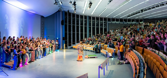 Panaromabild des 70ger Jahre Konzerts im Audimax. Links der Chor, rechts das Publikum, das begeistert mitklatscht.